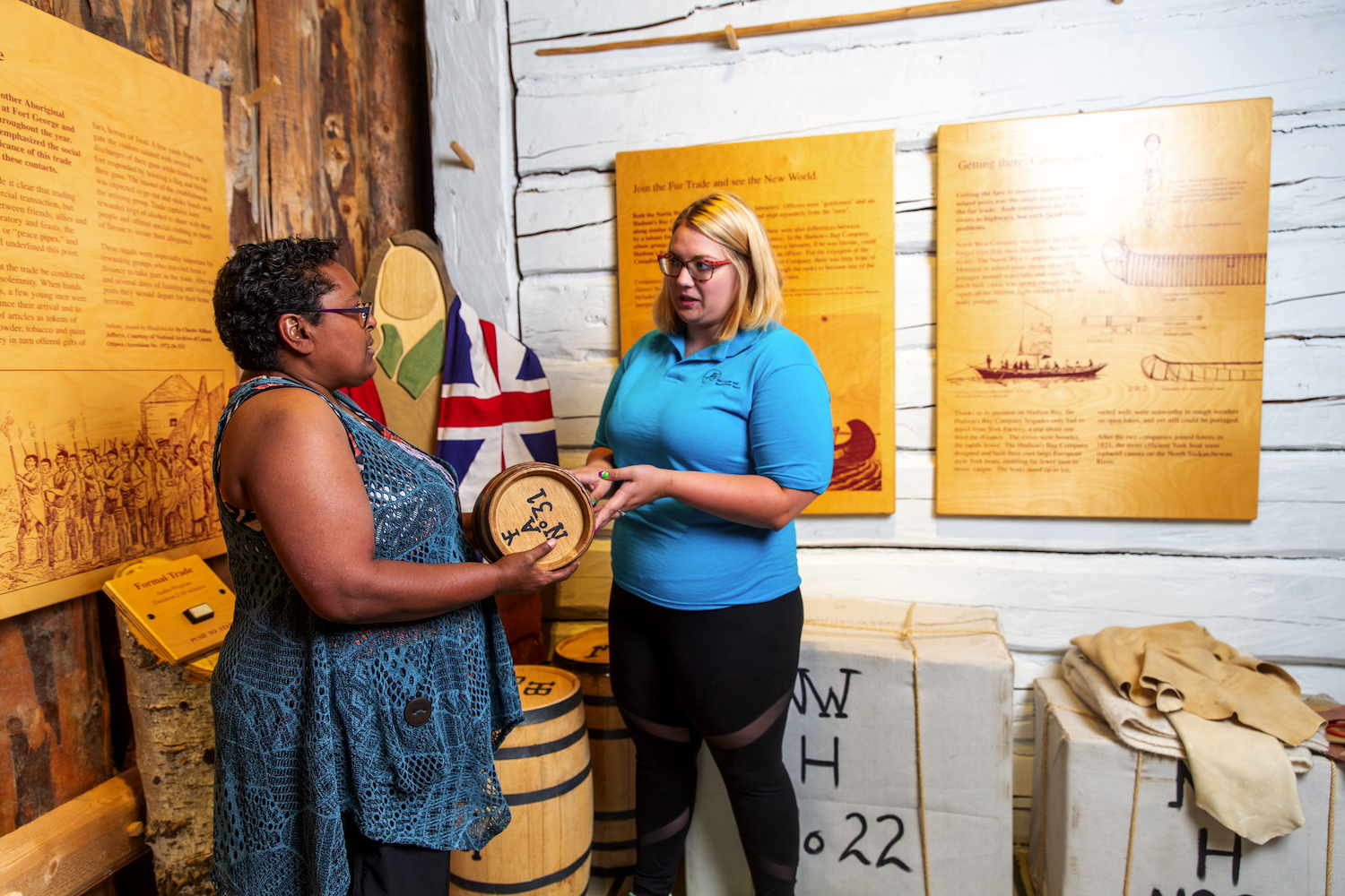 Standing inside the museum, a visitor holds a small barrel as an interpreter stands nearby.