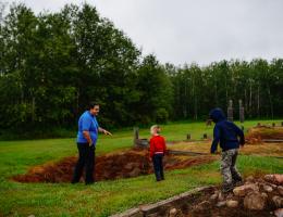 A historical interpreter and two young visitors examine an impression in the ground where a building once stood